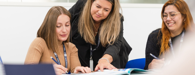 Lehrerin unterstützt zwei erwachsene Schülerinnen im Klassenzimmer während einer LISA! Sprachreise in Leeds