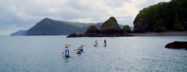 Englisch-Sprachreisen in England in Ilfracombe: Schueler beim Stand-Up-Paddeling im Meer vor traumhafter Kulisse.