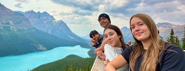 Jugendliche schauen in die Kamera, im Hintergrund ein See und hohe Berge der Rocky Mountains