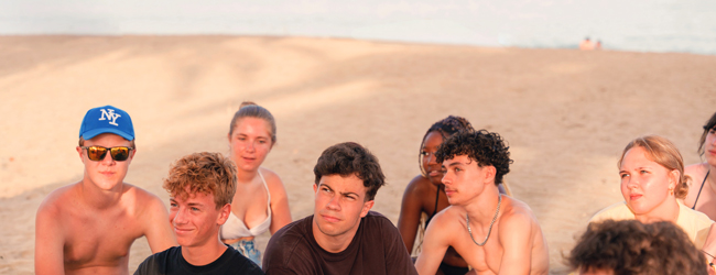 Mehrere Jugendliche sitzen im Sand am Strand von Barcelona und genießen die Abendsonne